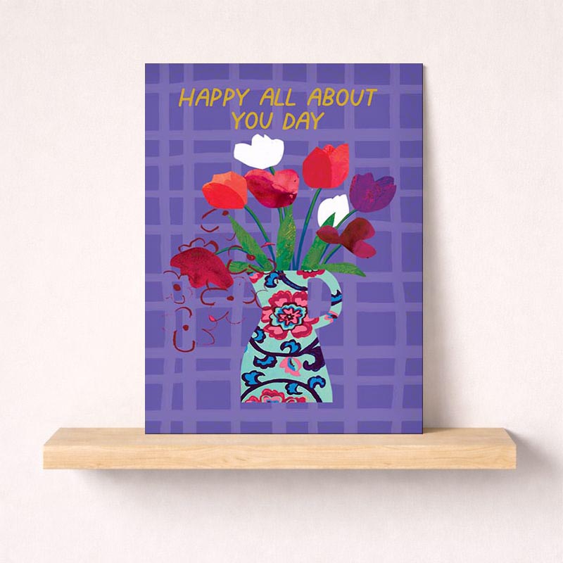 Brighten someone's day with a charming greetings card featuring a vase overflowing with vibrant flowers and a blue bird.