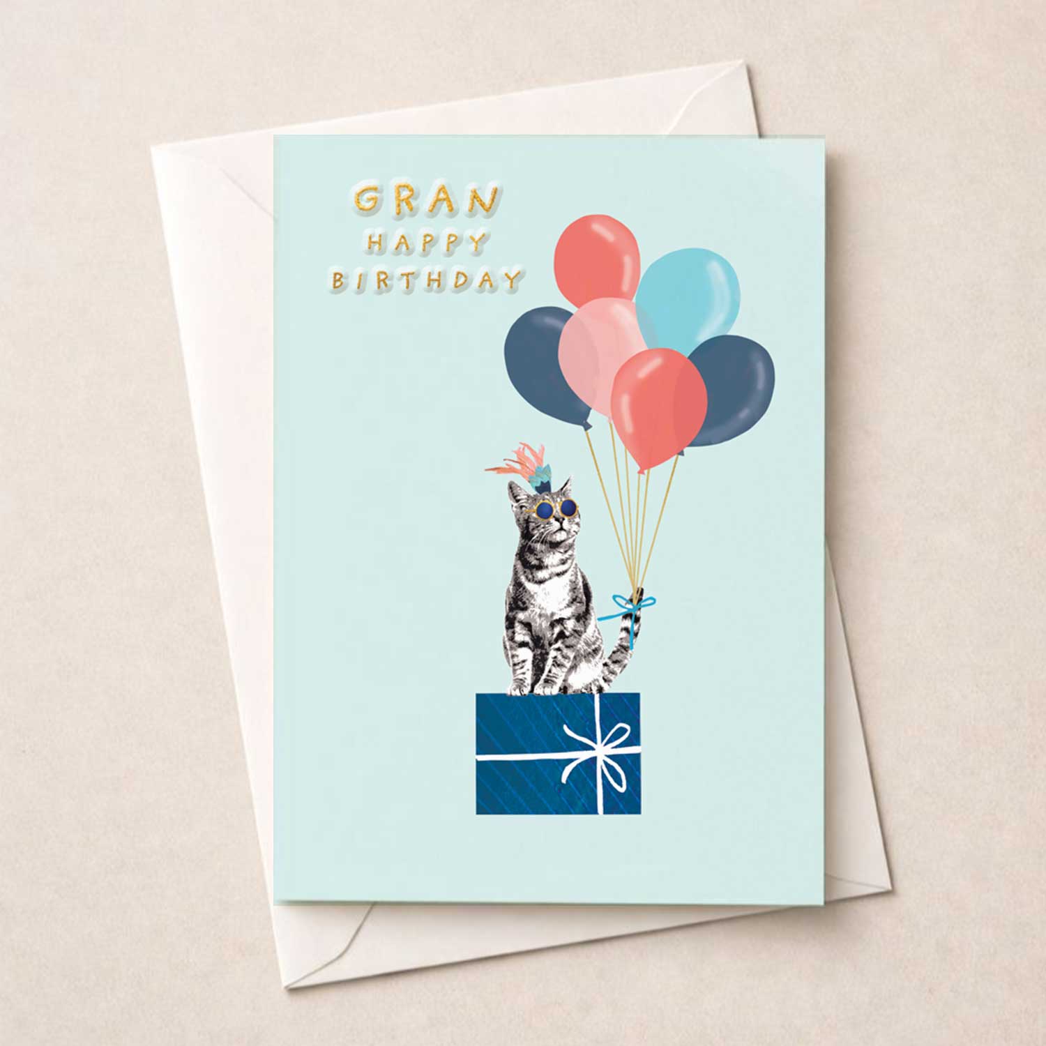 Birthday card for Gran featuring a cat wearing sunglasses and a party hat holding balloons on a pastel background