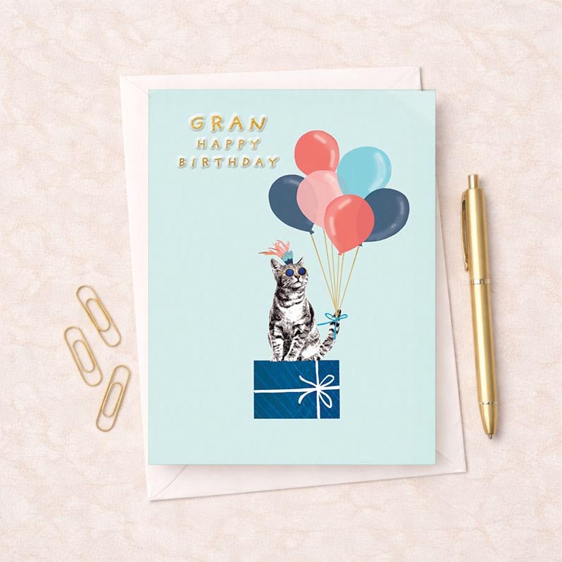 Birthday card for Gran featuring a cat wearing sunglasses and a party hat holding balloons on a pastel background