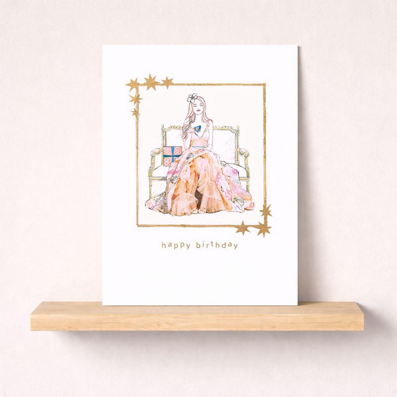 Charming birthday greetings card with woman on bed, pastel colours, "Happy Birthday" message. Perfect for showing you care.