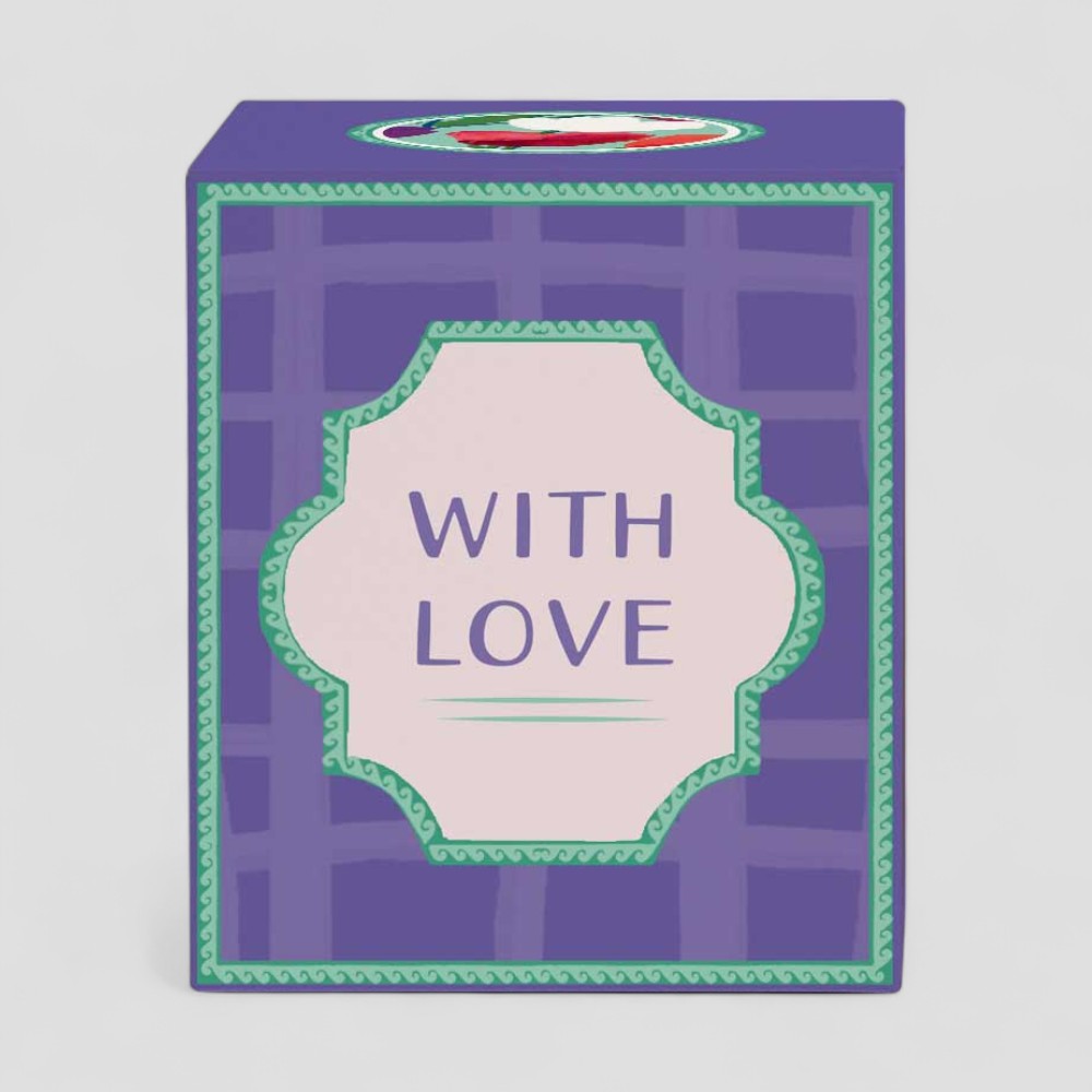 Lit yellow candle in glass with purple box labelled with love