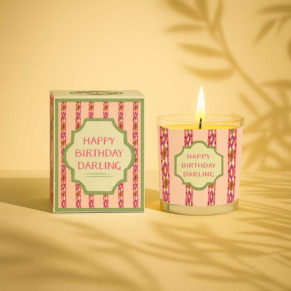 Lit birthday candle with decorative pink and green gift box and label reading Happy Birthday Darling
