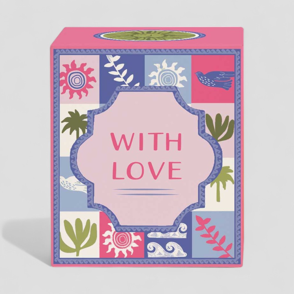 Lit yellow candle in glass with colourful patterned box labelled with love