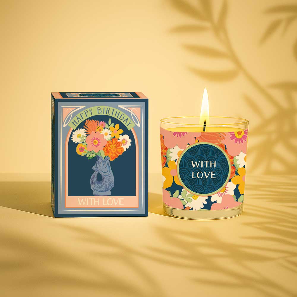 Lit yellow candle in glass with floral happy birthday gift box