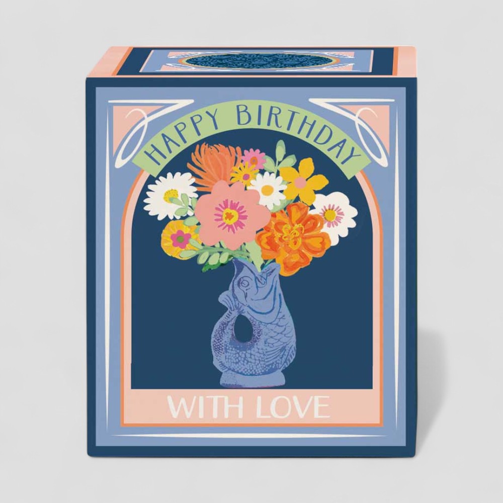 Lit yellow candle in glass with floral happy birthday gift box