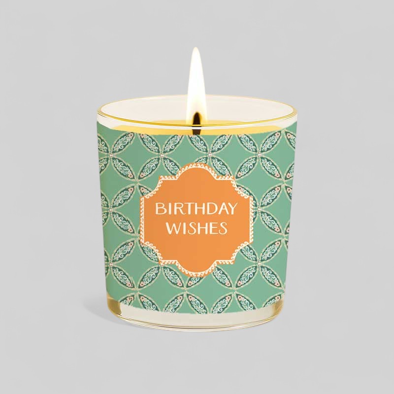 Lit yellow candle in glass with birthday wishes packaging and label