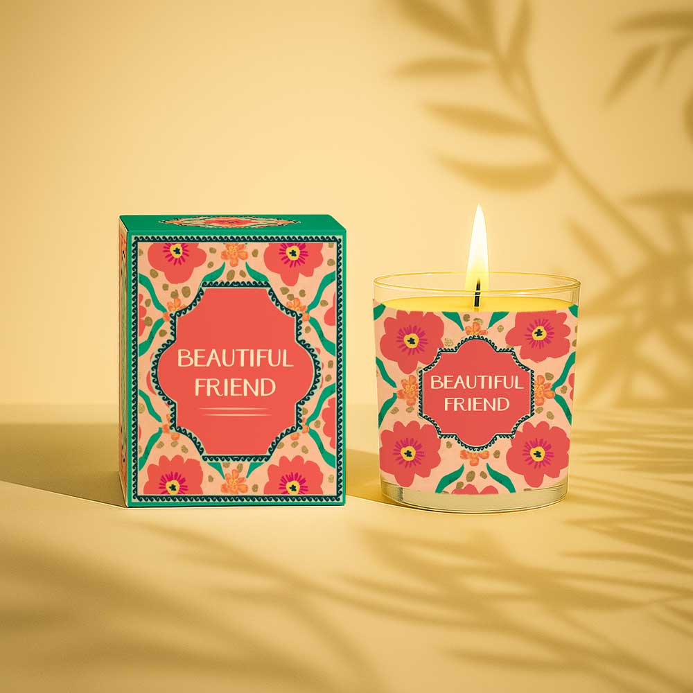 Lit yellow candle in glass with floral patterned beautiful friend box and label