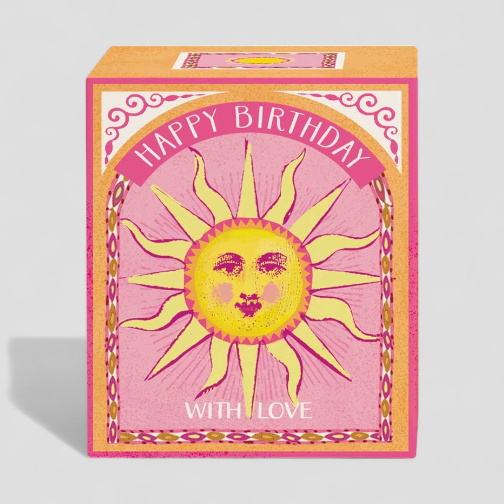 Lit yellow candle in glass with Happy Birthday gift box showing sun design