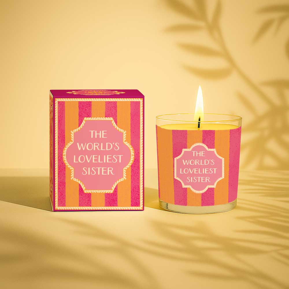 Lit yellow candle and matching box with the words The Worlds Loveliest Sister on plain background