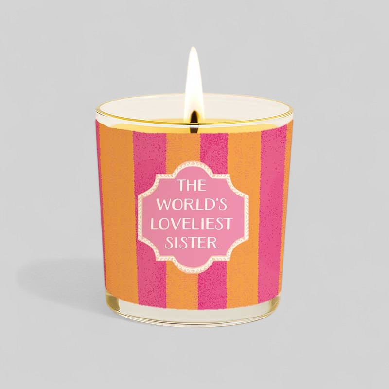 Lit yellow candle and matching box with the words The Worlds Loveliest Sister on plain background