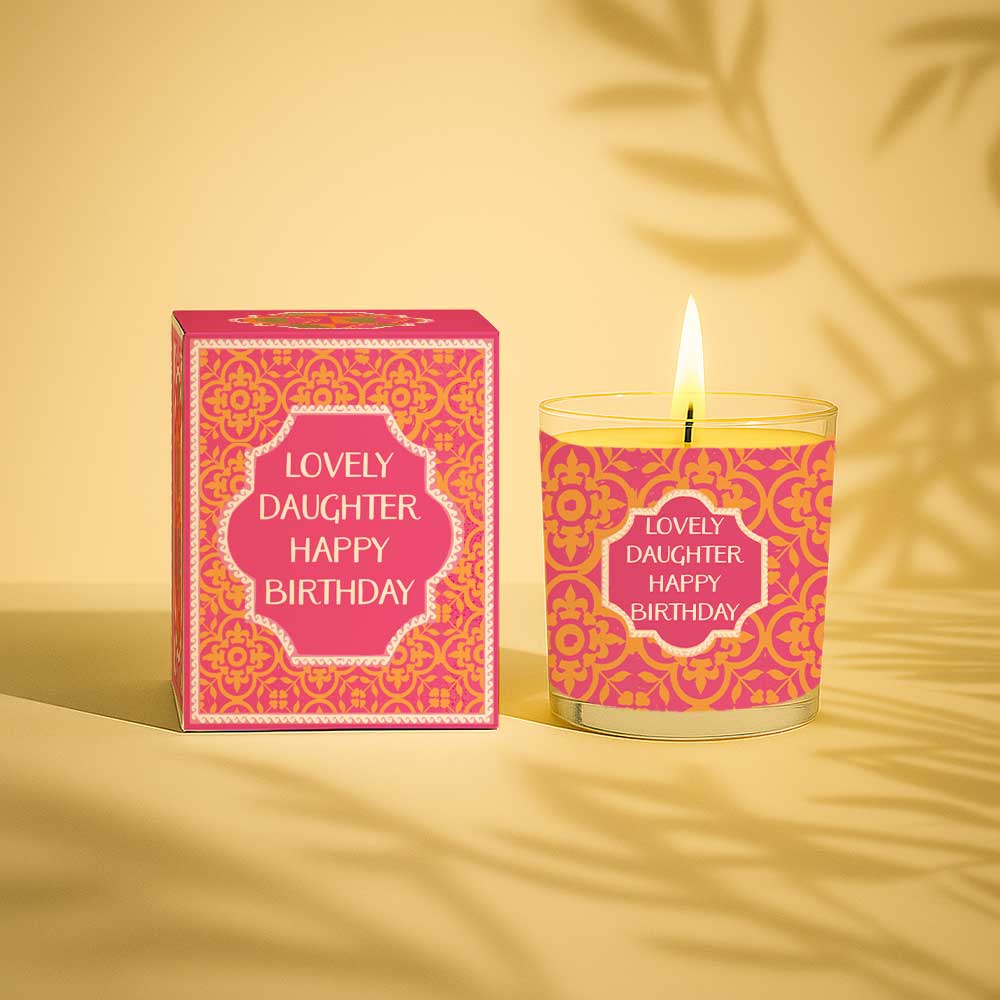 Burning yellow candle in glass with pink and gold birthday box for daughter