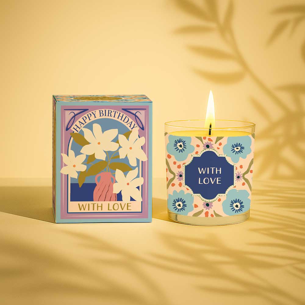 Lit yellow candle and floral birthday gift box with with love label