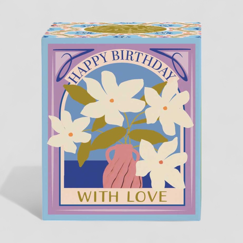 Lit yellow candle and floral birthday gift box with with love label