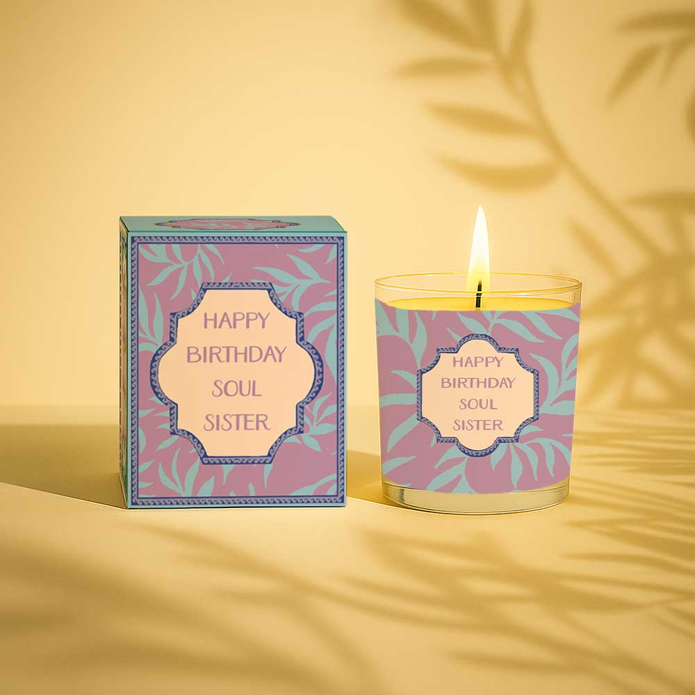 Lit yellow birthday candle in glass with purple and blue Happy Birthday Soul Sister box
