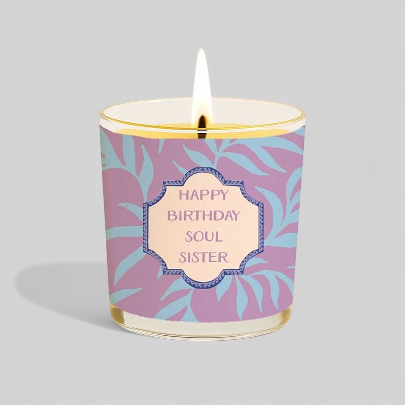Lit yellow birthday candle in glass with purple and blue Happy Birthday Soul Sister box