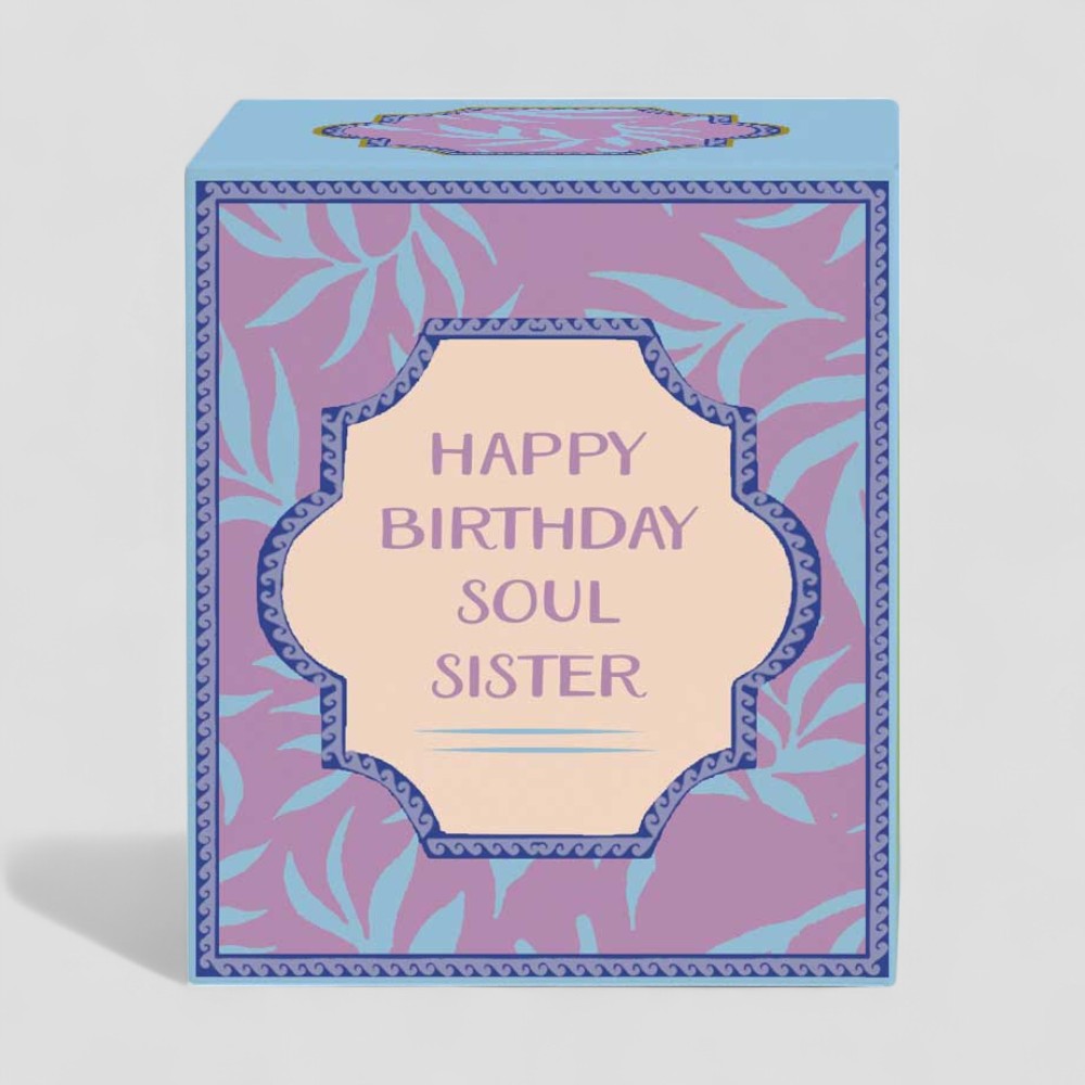 Lit yellow birthday candle in glass with purple and blue Happy Birthday Soul Sister box