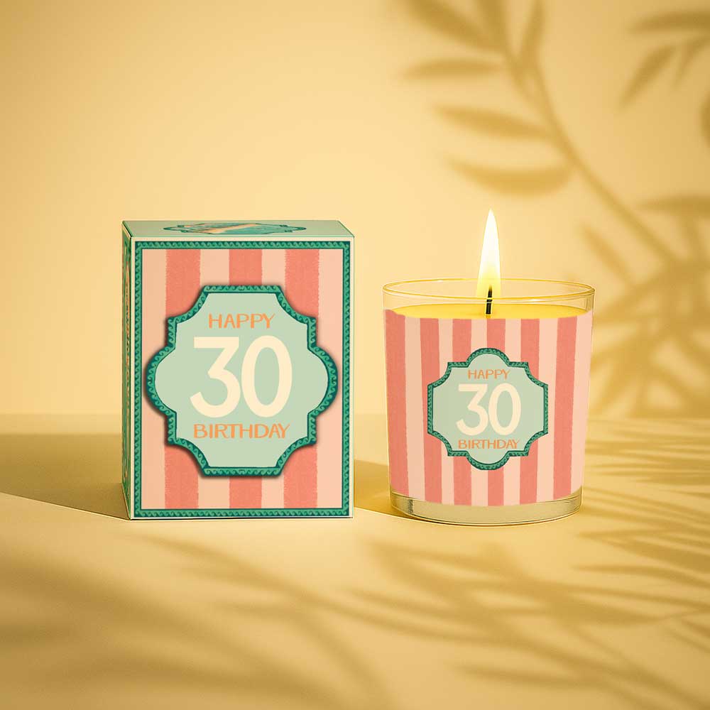 Lit yellow candle in glass with happy 30 birthday label and matching gift box
