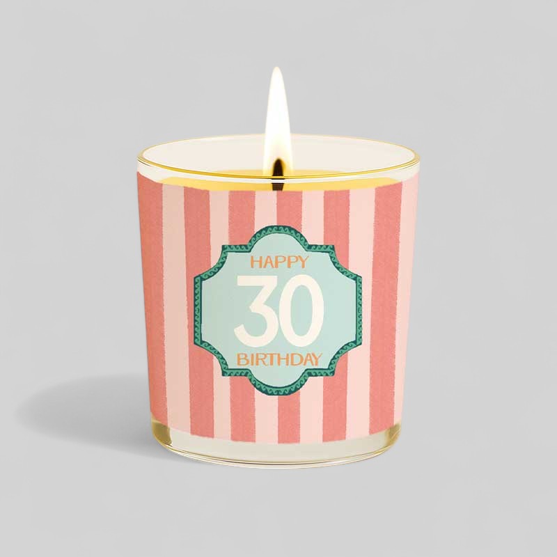 Lit yellow candle in glass with happy 30 birthday label and matching gift box