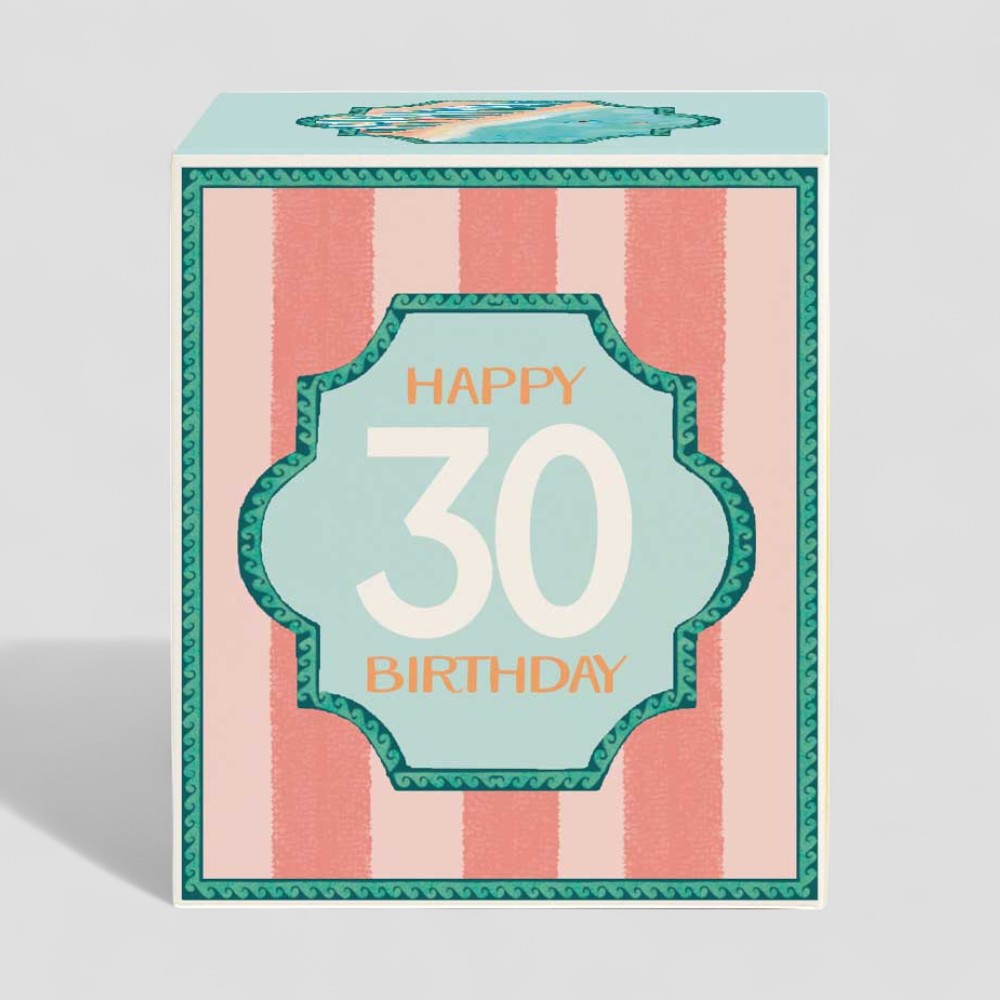 Lit yellow candle in glass with happy 30 birthday label and matching gift box
