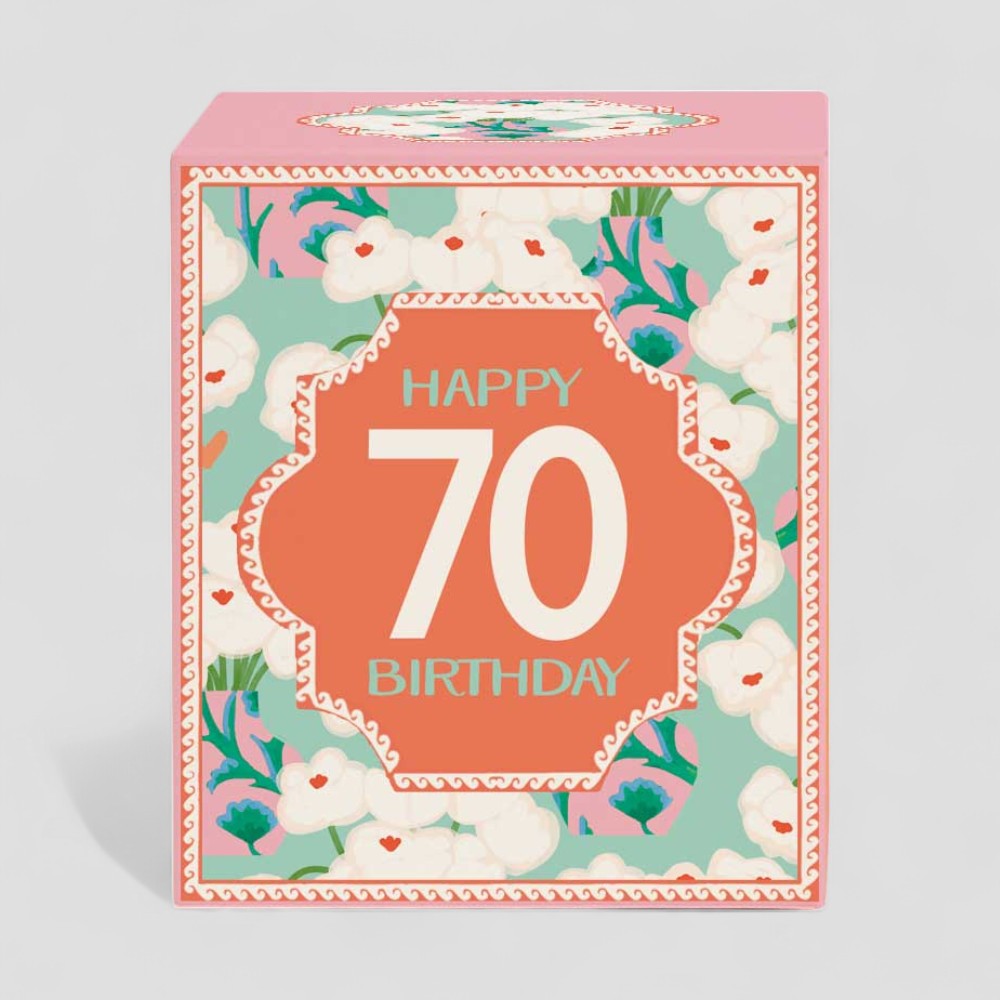 Lit yellow candle with happy 70 birthday label next to matching floral gift box
