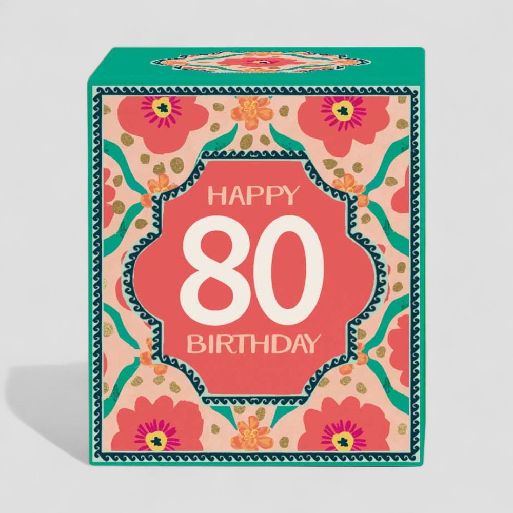 Lit yellow candle and box with floral design and Happy 80 Birthday text