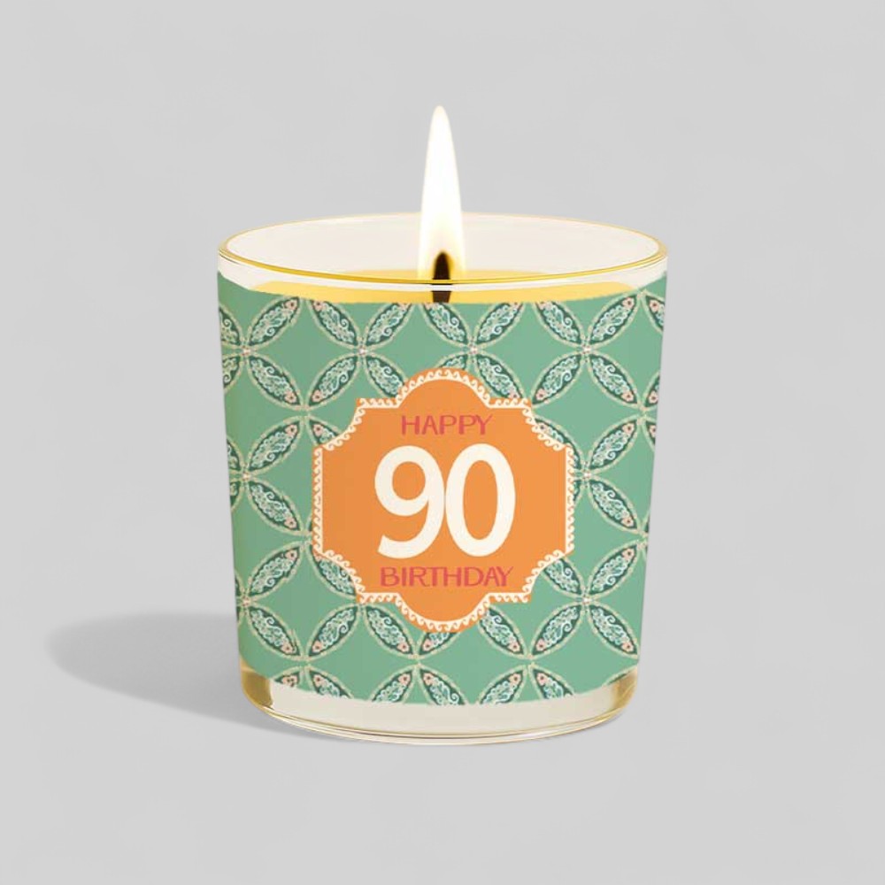 Lit yellow candle with happy 90th birthday label beside matching gift box