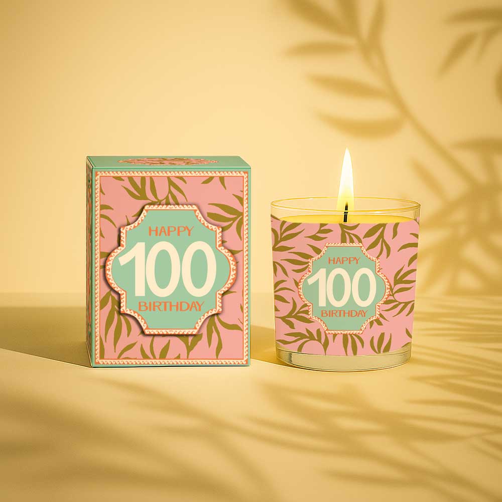 Lit yellow candle in glass with 100 birthday design and matching decorative box