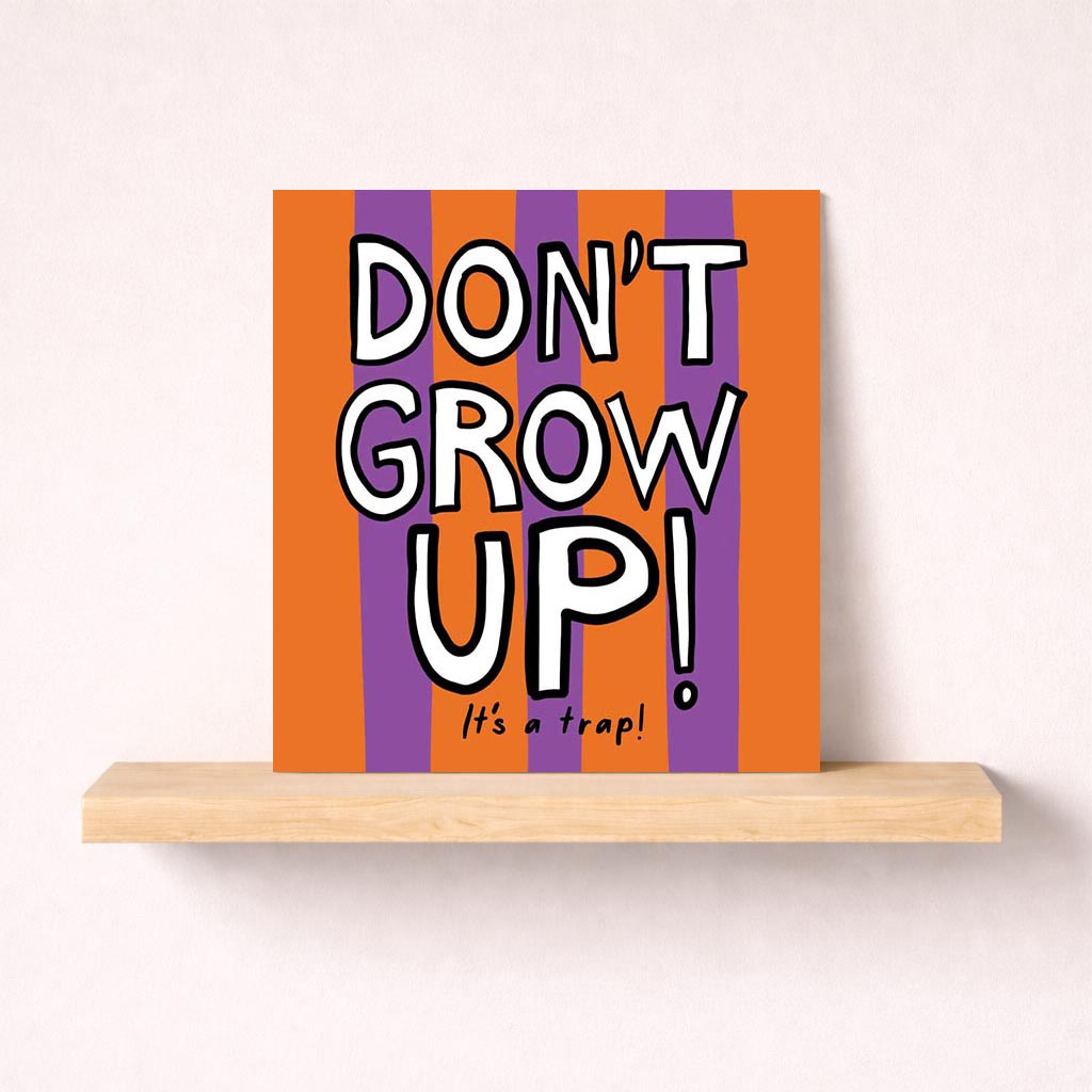 Colorful card with bold text saying "DON'T GROW UP! It's a trap!" against purple and orange background. Perfect for birthdays or graduations.