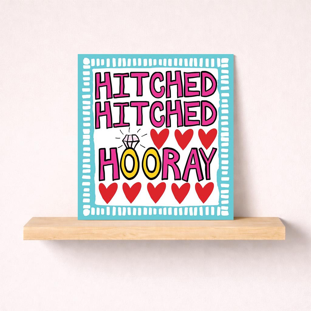 A charming greetings card with "HITCHED HOORAY" message, perfect for celebrating love and weddings. Hand-drawn sign with ring and hearts adds romance.
