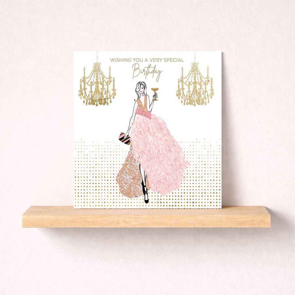 Elegant greetings card with woman in pink dress holding wine glass, gold glitter chandelier. Chic and stylish for special occasions.