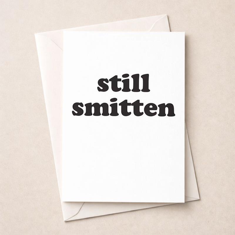 Romantic black and white greetings card with 'still smitten' in elegant typography. Ideal for expressing love to a special someone.