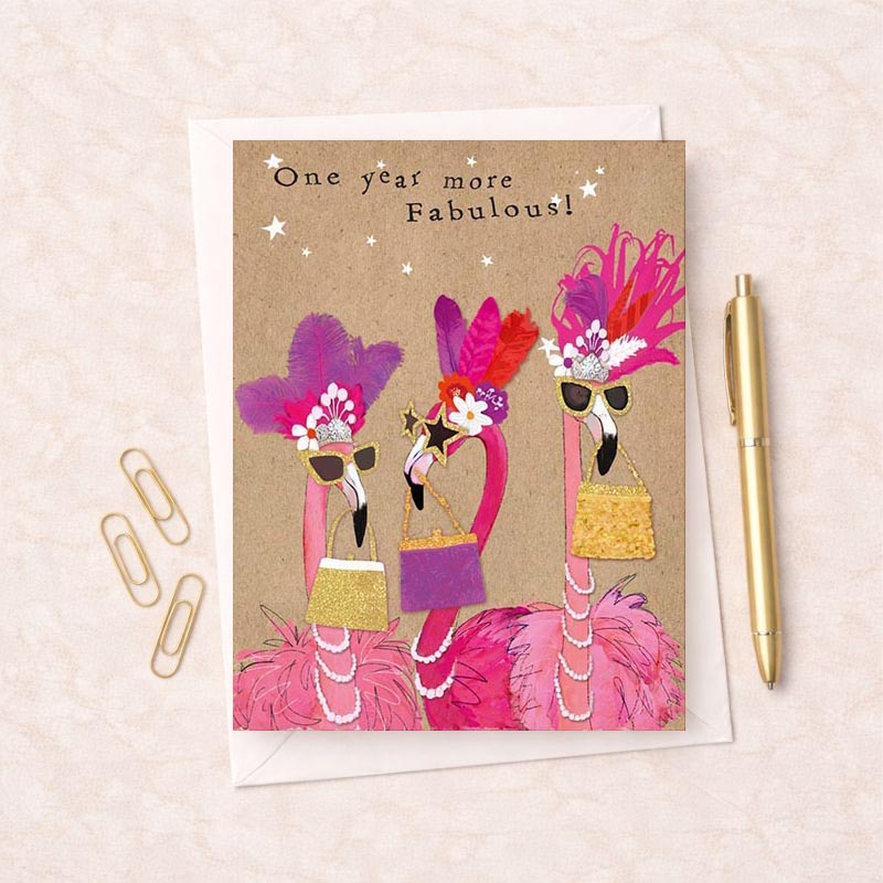Three flamboyant flamingos in fancy outfits, hats, purses, and pearls on a charming greetings card. Ideal for birthday wishes and special occasions.