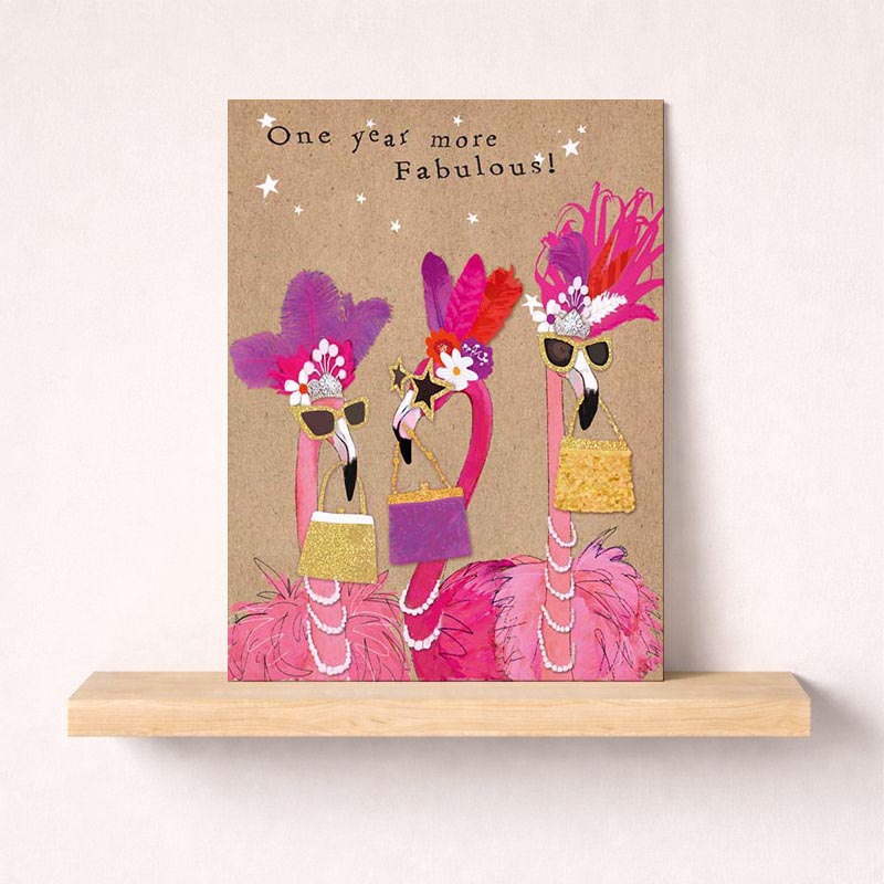 Three flamboyant flamingos in fancy outfits, hats, purses, and pearls on a charming greetings card. Ideal for birthday wishes and special occasions.