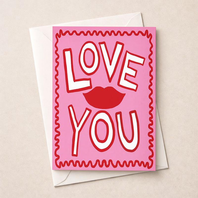 Pink greetings card with red and white "love you" sign, perfect for expressing love and affection on various occasions.