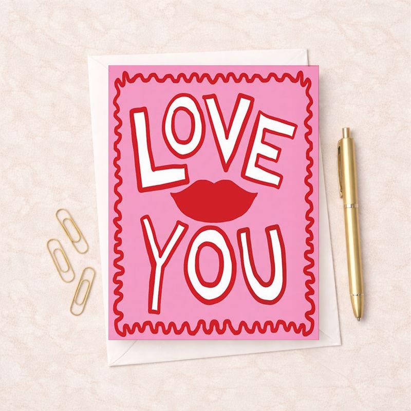 Pink greetings card with red and white "love you" sign, perfect for expressing love and affection on various occasions.