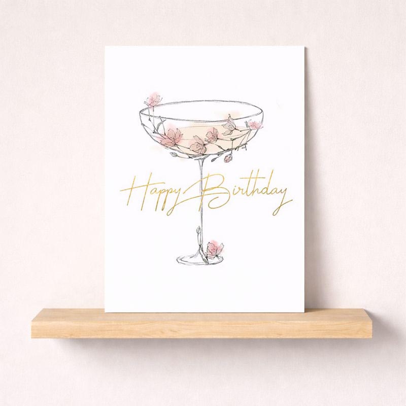A charming greetings card with a drawing of a glass adorned with flowers, exuding warmth and cheer. Perfect for birthdays and anniversaries.
