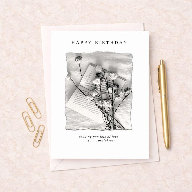 A charming greetings card with a book and flowers on a white sheet, perfect for book lovers or nature enthusiasts.