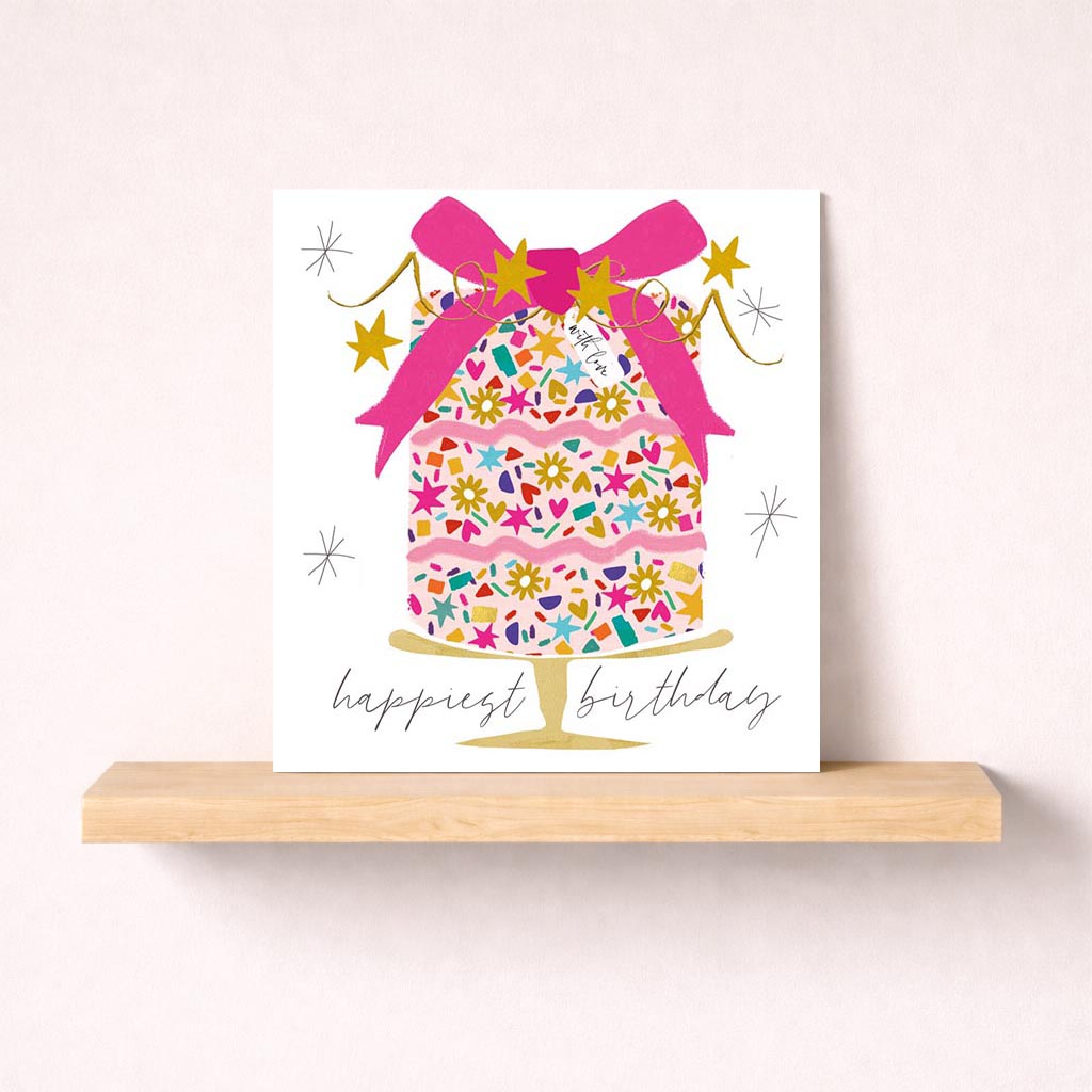 Whimsical cake with pink bow, stars, and love written in elegant script on a birthday greetings card.